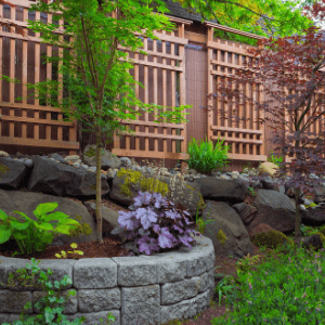backyard landscaping - a retaining wall with a circular raised flower bed stops soil erosion from steep adjacent property
